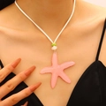 Elegant pink starfish pendant necklace on a white cord worn by a model for a summer look - Pink (6592)