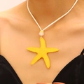 Detail view of a vibrant yellow starfish pendant necklace worn on a white cord. - Yellow (6736)