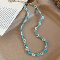 Detailed view of a handmade blue and white beaded flower necklace with gold accents on a tray. - Necklace / White-Blue