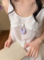 Close-up of a purple ribbed oval pendant on a white cord necklace worn by a model - Purple