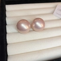 Close-up view of elegant large pink pearl stud earrings on a white jewelry display tray. - Pink