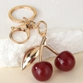 Chic dark red cherry keychain with gold-plated metal clasp on minimalist stone background - Burgundy