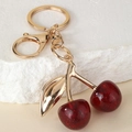 Fashionable cherry keychain with red resin fruit and gold metal leaf on white stone background - Glitter Wine Red