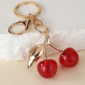 Macro shot of red glitter cherry keychain with gold leaf detail on a textured stone - Glitter Red