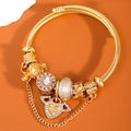 Golden open cable bangle with winged heart and crown charms on an orange background - White