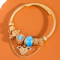 Elegant gold twisted bangle with blue rhinestones, beads and angel heart wing charms - Blue