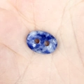 Macro view of a blue marble oval gemstone bead with double holes held in hand - 10*14*4mm / Sodalite