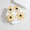 Golden hollow flower earrings with black bead center on white geometric display stand - Black Stone Flower Style (E745-B)