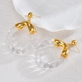 Twisted texture golden metal and clear acrylic round hoop earrings on a white ceramic plate - White