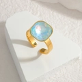 Elegant gold square ring with iridescent light blue gemstone on stone stand - Blue