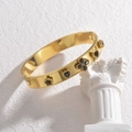Goldener Edelstahlarmreif mit schwarzen Kleeblatt-Anhängern auf weißer Säule - Schwarzer Zirkonia-Stil