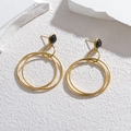 Elegant gold geometric drop earrings with black stones on a minimalist stone background - Gold
