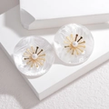 Macro detail of pearl stud earrings with golden flower centers on white stone display - White