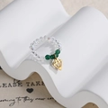 Detail of beaded elastic ring with green accents and gold geometric charm on a stand - Clear and Green Beaded Diamond Style