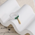 Macro detail of elastic beaded ring featuring green beads and golden feather pendant - Clear and Green Beaded Feather Style