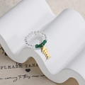 Close-up of beaded ring with transparent crystals, green stones, and gold fishbone charm - Clear and Green Beaded Fishbone Style