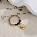 Detail of beaded ring with gold lock charm and black faceted beads on textured background - Gold and Black Beaded Lock Style