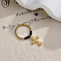 Macro detail of elastic beaded ring with black faceted beads and gold cross charm - Gold and Black Beaded Cross Style