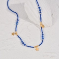 Detail of blue beaded necklace with gold star pendants on a textured white stone surface - Deep Blue Beaded Star Pendant Style (N1937-sl)
