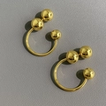 Gold C-shaped metallic ball earrings with mirror polish finish on dark leather - Gold