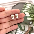 Macro shot of polished C-shaped silver earrings held against a floral lifestyle backdrop - Silver Style