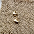 Detailopname van gepolijste gouden croissant oorbellen op een getextureerde stoffen ondergrond - Gouden Kleine Maan