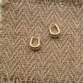 Detail van elegante gouden U-vormige creolen op een getextureerde bruine stoffen - Gouden U-ring