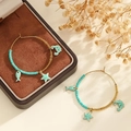 Détail de créoles dorées avec perles turquoise et breloques étoile de mer sur boîte - Bleu lac