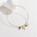 Bracciale placcato oro 18K con ciondoli a croce, perla e pietre su sfondo materico - Stile Perla Croce Minerale Blu Scuro