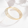 Close-up van drie minimalistische 2mm vergulde roestvrijstalen armbanden op een witte voet - Gouden Minimalistisch Glad (CXB1251-02)