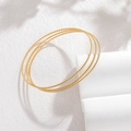 Detailopname van drie 2mm gouden gedraaide armbanden op een witte display - Gouden Gedraaide Touw Textuur (CXB1250-02)