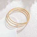 Detail van drie minimalistische goudkleurige roestvrijstalen armbanden met textuur - Gouden Micro Geëtste Textuur (CXB1249-02)