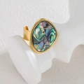 Unregelmäßiger geometrischer Ring mit ovaler Abalone-Muschel auf weißem Präsentationsständer - Gold mit Bunter Abalone-Muschel