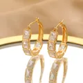 Close-up of gold-plated hoop earrings with rectangular gemstones on a mirror - Gold