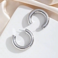 Detailed close-up of large chunky silver-finish C-shape hoop earrings on elegant satin - Silver