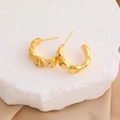 Detail of 18K gold-plated C-shaped hoop earrings with textured fan patterns on a white stone - 18K Gold / Gold