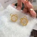 Gros plan de boucles d'oreilles nœuds dorés tenues sur un tissu en peluche blanc - Doré