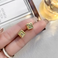 Detailed view of a square gold earring with a purple zircon stone held by a person - Square Cross Star Zircon Style (A0630C) / 24K / Gold