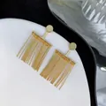 Dettaglio di orecchini pendenti a nappa geometrici dorati su un piatto di ceramica bianca - Oro (A0718B)