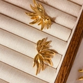 Close-up of golden angel wing earrings with feathered texture on beige velvet - Gold