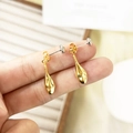 Detalle de pendientes de gota dorados con acabado metálico brillante sujetos a mano - Gota de oro con pin de plata (A0335B)