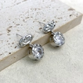 Macro shot of silver fluid-texture earrings with round diamond-cut zircon drops on stone - Silver