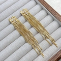 Nahaufnahme von goldenen Quastenohrringen mit Strasssteinen auf grauer Box - Lange geometrische Gitter-Quaste Gold (A1004-07C)