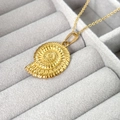 Makroaufnahme eines goldenen Muschel-Anhängers mit Textur auf grauem Samthintergrund - Gold Nautilus Stil (A1002-10C)