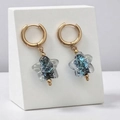 Detail van gouden ster-oorbellen met blauw glitterglas op witte standaarden - Iriserende Blauwe Ster