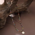 Bunte Perlenkette mit goldenem Blumenanhänger auf rustikalem Holz im schicken Boho-Stil - Rosen-Sonnenblumen-Stil