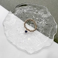 Close-up of golden beaded stretch ring with a hanging heart-shaped blue gemstone charm - Gold-Blue Zirconia