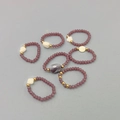 Dettaglio di 7 anelli elastici con perline viola, accenti dorati e ciondoli a cuore - Set da 7 pezzi