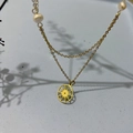 Détail du collier doré double couche motif soleil avec perles sur fond bleu clair - Soleil de Perle Dorée (DN088)