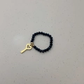 Detail van elastische ring met zwarte gefacetteerde kralen en goudkleurige hart-sleutel hanger - Sleutelhanger / Zwarte Kraal